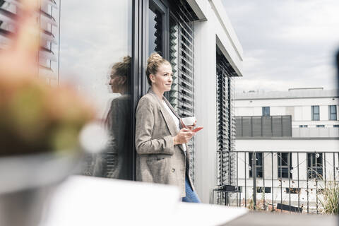 Geschäftsfrau mit Mobiltelefon und Kaffeetasse auf der Dachterrasse, lizenzfreies Stockfoto