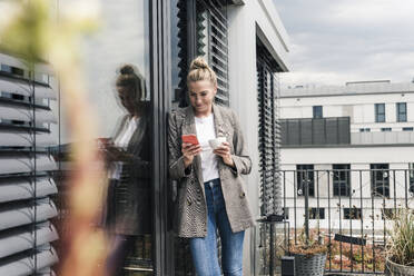 Geschäftsfrau mit Mobiltelefon und Kaffeetasse auf der Dachterrasse - UUF18574