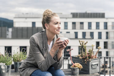 Businesswoman with coffee cup sitting on roof terrace having a break - UUF18577