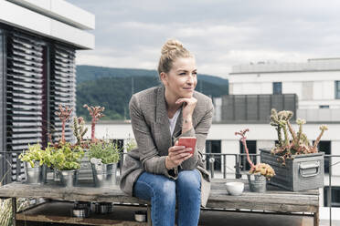 Geschäftsfrau mit Mobiltelefon auf der Dachterrasse sitzend und eine Pause machend - UUF18578