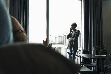 Geschäftsfrau mit Mobiltelefon am Fenster im Büro stehend - UUF18579