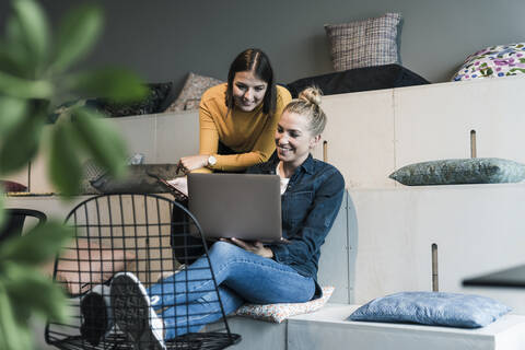 Zwei lächelnde Geschäftsfrauen benutzen einen Laptop in einer Bürolounge, lizenzfreies Stockfoto