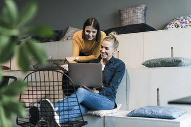 Zwei lächelnde Geschäftsfrauen benutzen einen Laptop in einer Bürolounge - UUF18583