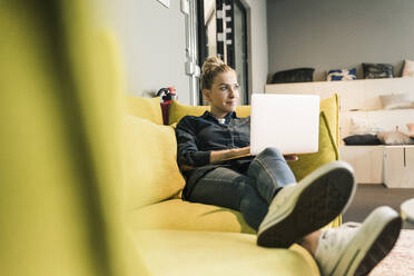 Lässige Geschäftsfrau mit Laptop auf der Couch in der Büro-Lounge - UUF18584