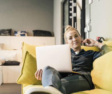 Lässige Geschäftsfrau mit Laptop auf der Couch in der Büro-Lounge - UUF18587