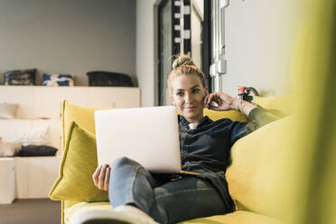 Lässige Geschäftsfrau mit Laptop auf der Couch in der Büro-Lounge - UUF18588