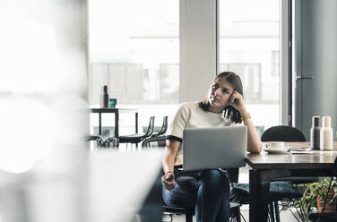 Serious casual businesswoman with laptop at desk in office - UUF18593