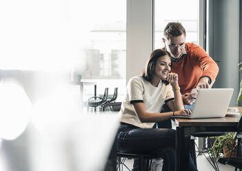 Casual businessman and woman with laptop meeting in office - UUF18594