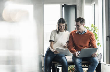 Casual businessman and woman with laptop and documents meeting in office - UUF18598