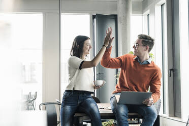 Happy casual businessman and woman high fiving in office - UUF18599