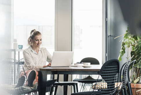 Geschäftsfrau sitzt am Tisch im Büro und benutzt einen Laptop - UUF18609