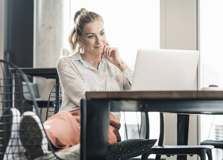 Geschäftsfrau sitzt am Tisch im Büro und benutzt einen Laptop - UUF18611