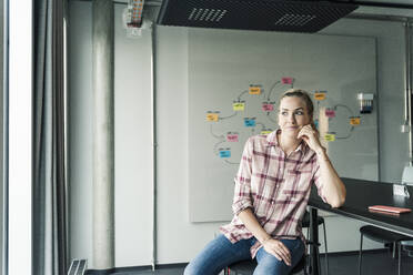 Lässige Geschäftsfrau sitzt im Büro mit Mind Map im Hintergrund - UUF18630