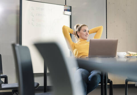 Lässige Geschäftsfrau sitzt am Tisch im Konferenzraum und lehnt sich zurück, lizenzfreies Stockfoto