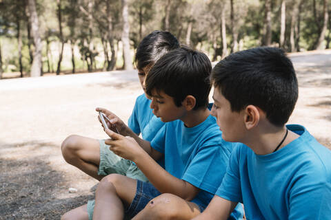 Drei Jungen in blauen T-Shirts benutzen Smartphone, lizenzfreies Stockfoto