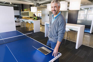 Businessman using laptop at table tennis table in office - BLEF13983