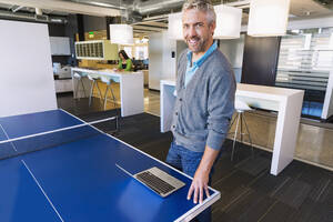 Geschäftsmann mit Laptop an der Tischtennisplatte im Büro - BLEF13983
