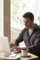 Mann mit Laptop und einer Tasse Kaffee in einem Cafe - BLEF14053
