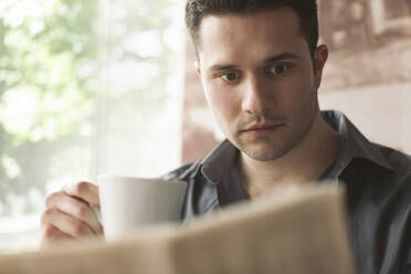 Man drinking cup of coffee and reading newspaper - BLEF14056