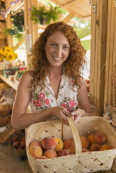 Caucasian woman basket of peaches at farmers market - BLEF14063