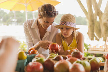 Mixed race mother and daughter browsing produce at farmers market - BLEF14084