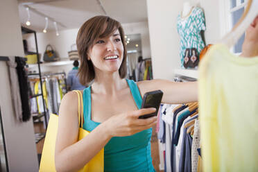 Hispanic woman taking picture of shirt in clothing store - BLEF14179