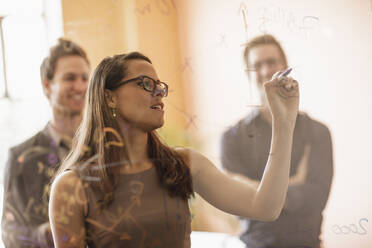 Mixed race businesswoman writing on glass wall - BLEF14188