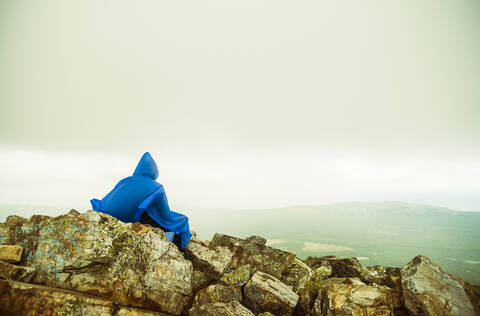 Kaukasischer Wanderer auf felsiger Bergkuppe sitzend, lizenzfreies Stockfoto