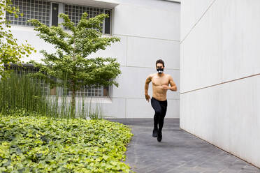 Junge Athletin beim intensiven Lauftraining in der Stadt, mit Atemmaske - MAUF02735