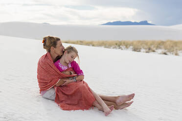 Caucasian mother and daughter wrapped in blanket on sand dune - BLEF14207