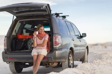 Caucasian woman leaning on car drinking coffee - BLEF14214