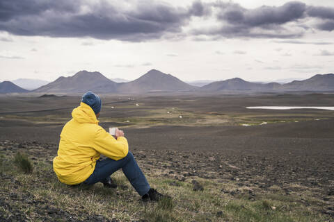 Mann trinkt Kaffee und betrachtet die Landschaft in Island, lizenzfreies Stockfoto