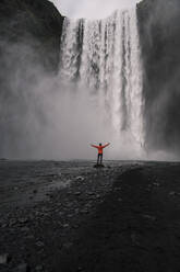 Älterer Mann vor den Skogafoss-Wasserfällen mit erhobenen Armen, Island - UUF18664