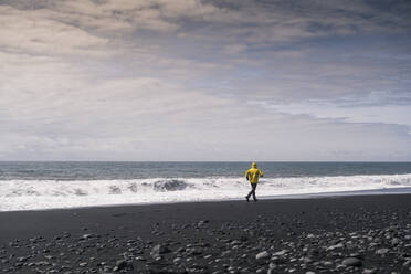 Mature man running on a lava beach in Iceland - UUF18671