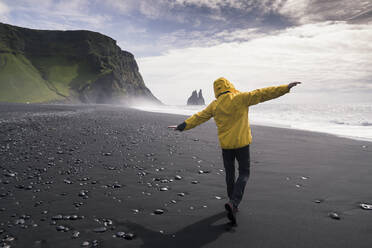 Mature man walking on a lava beach in Iceland, with arms outstretched - UUF18675