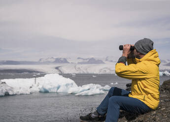 Mature man watching Vatnajokull glacier with binoculars, Iceland - UUF18702