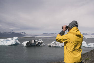 Mature man watching Vatnajokull glacier with binoculars, Iceland - UUF18705