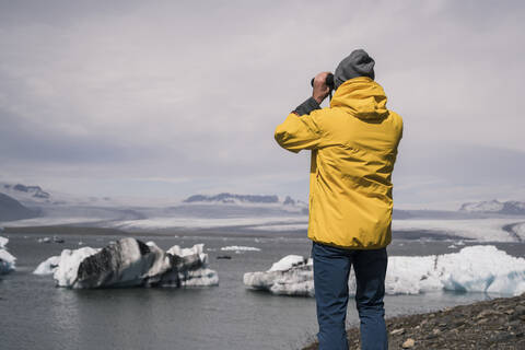 Älterer Mann beobachtet den Vatnajokull-Gletscher mit einem Fernglas, Island, lizenzfreies Stockfoto