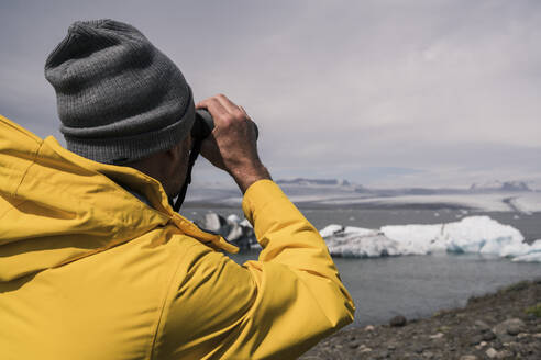 Mature man watching Vatnajokull glacier with binoculars, Iceland - UUF18707