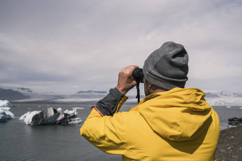 Mature man watching Vatnajokull glacier with binoculars, Iceland - UUF18708