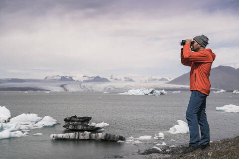 Älterer Mann beobachtet den Vatnajokull-Gletscher mit einem Fernglas, Island, lizenzfreies Stockfoto