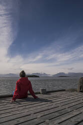 Young woman sitting on a jetty, looking at the sea, South East Iceland - UUF18730