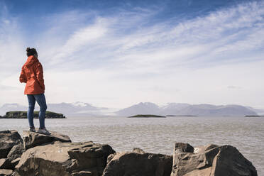 Junge Frau steht auf Felsen und blickt auf das Meer, Südostisland - UUF18735