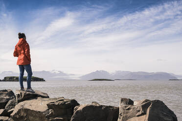 Young woman standig boulders, looking at the sea, South East Iceland - UUF18735