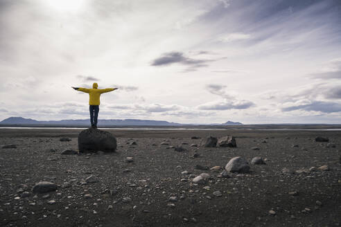 Mature man standing on a rock in the volcanic highlands of Iceland with arms out - UUF18769