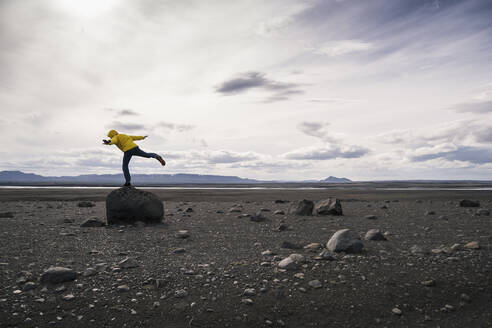 Mature man balancing on one leg on a rock in the volcanic highlands of Iceland - UUF18770