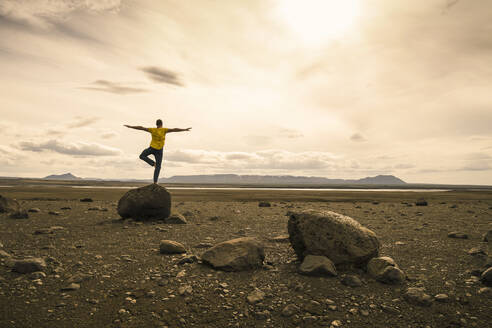 Mature man balancing on one leg on a rock in the volcanic highlands of Iceland - UUF18773