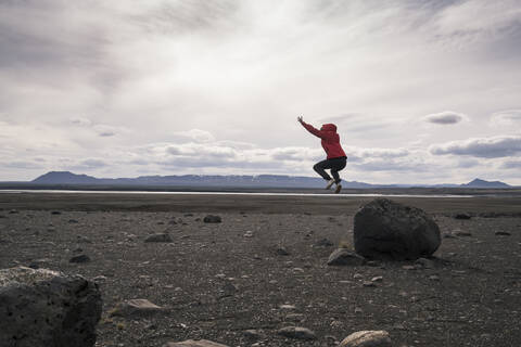 Junge Frau springt von einem Felsen im vulkanischen Hochland von Island, lizenzfreies Stockfoto