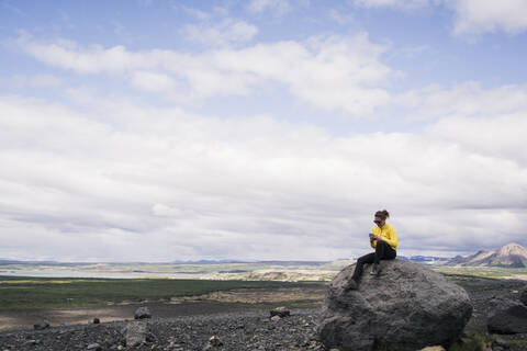 Young woman sitting on rock at Myvatn, Iceland, using smartphone stock photo