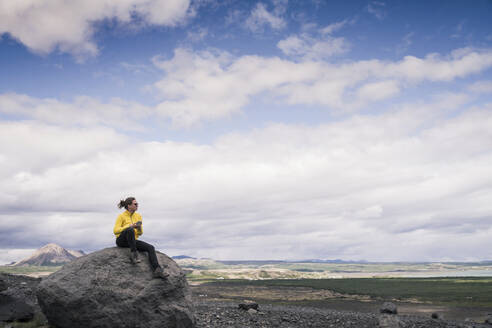 Junge Frau sitzt auf einem Felsen am Myvatn, Island, und benutzt ein Smartphone - UUF18790